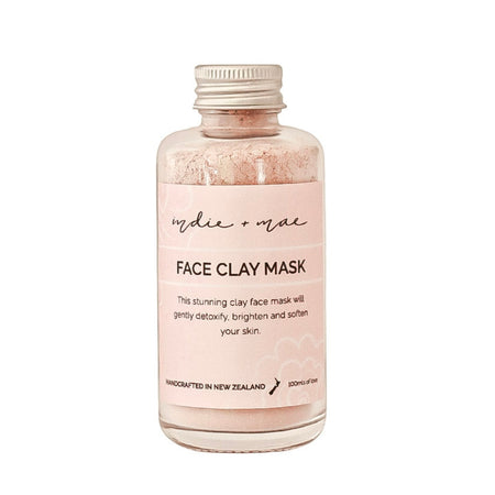A clear glass bottle of 'indie or not' Face Clay Mask with a light pink label and a silver metal cap, containing a light pink clay powder, shown on a plain white background.