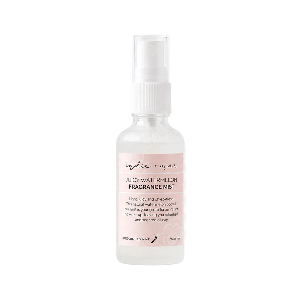 A clear spray bottle of Iggie & Mine Lacy Watermelon Fragrance Mist with a white spray top and a light pink label, shown on a white and gray checkered background.