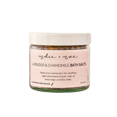 A jar of 'indie o mare' Lavender & Chamomile Bath Salts on a solid white background. The product features a white lid, a light pink label with black text, and a clear glass container showing the herbal bath salts inside.