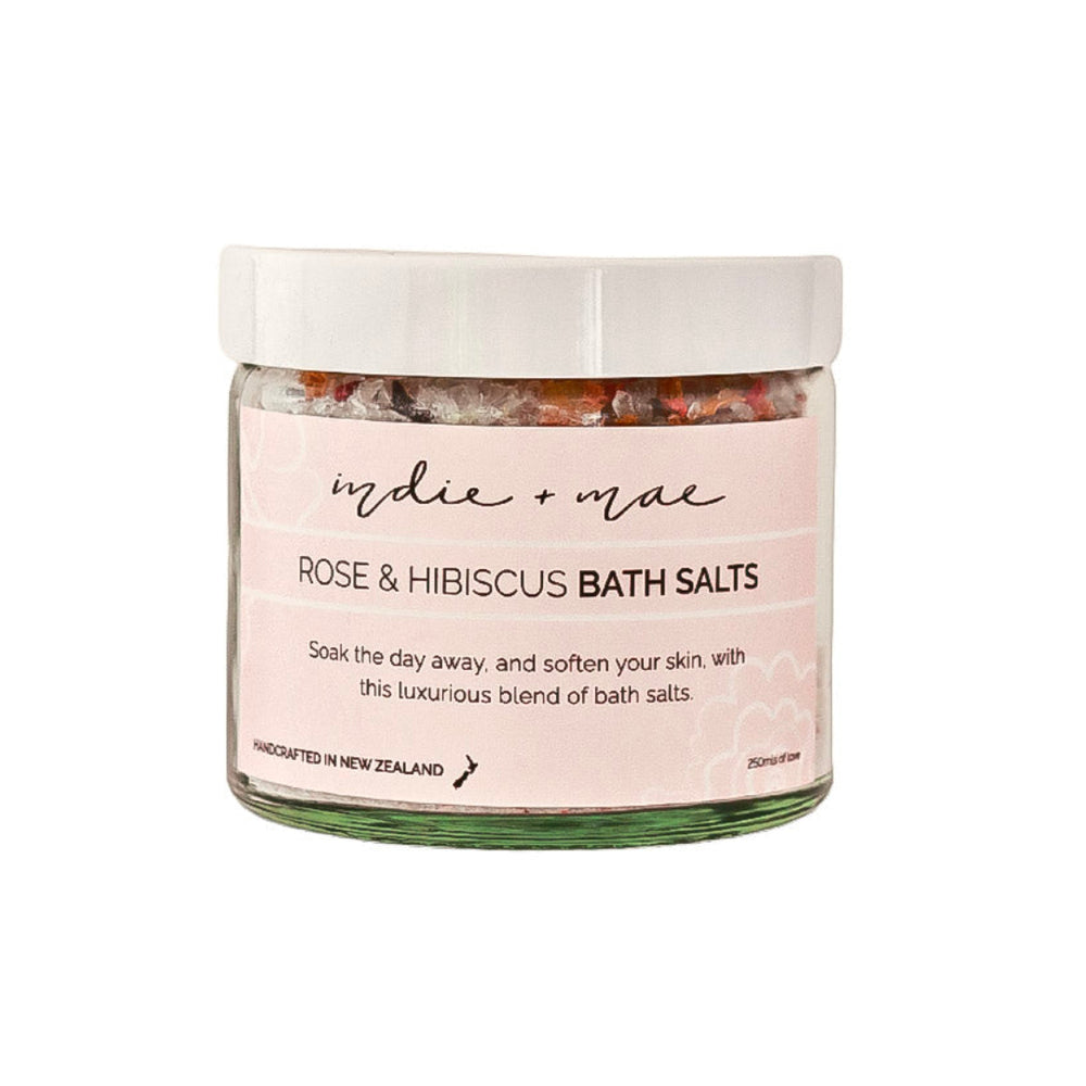 A glass jar of 'indie + mac' Rose & Hibiscus Bath Salts with a white lid and a light pink label, set against a plain white background.
