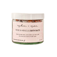A glass jar of 'indie + mac' Rose & Hibiscus Bath Salts with a white lid and a light pink label, set against a plain white background.