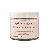 A jar of 'sydnie & mae' Rose & Peony Body Polish on a clean white background. The product is in a clear glass jar showing a pale pink polish inside, topped with a white lid and a white label with black text.
